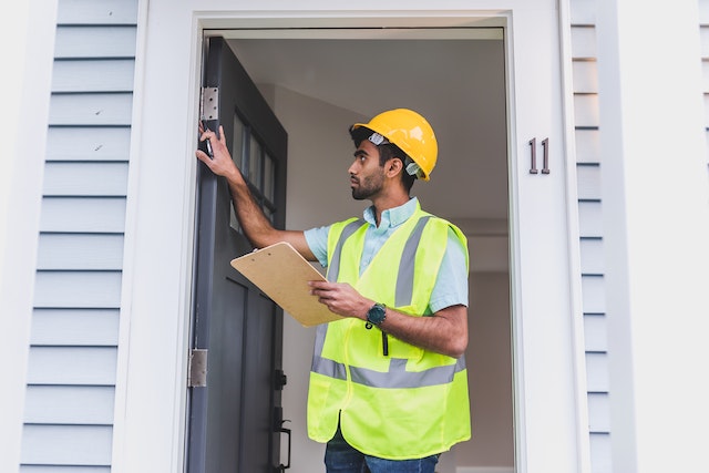 staff in a yellow vest and a hard hat looking at a home's doorway